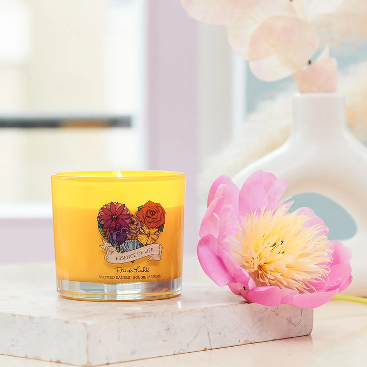 Frida Kahlo Essence of Life scented candle. Bright yellow glass candle featuring a colorful floral design and elegant Frida Kahlo branding on the front.