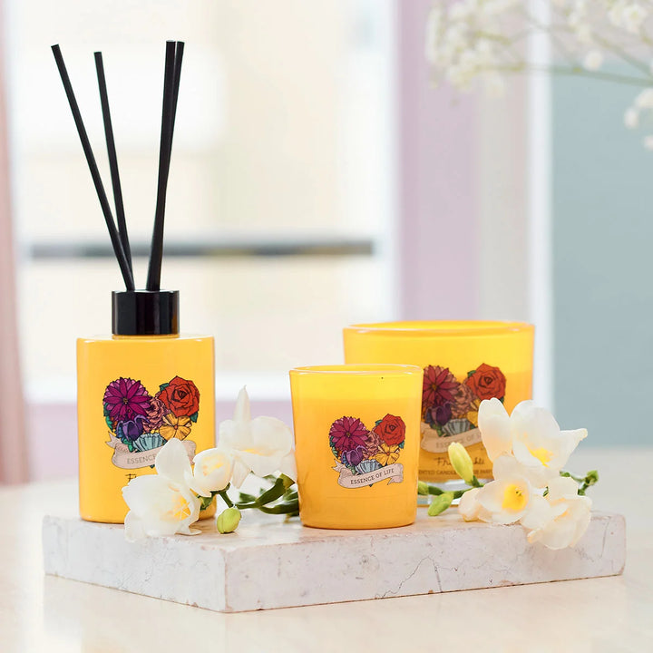 Frida Kahlo Essence of Life scented candle. Bright yellow glass candle featuring a colorful floral design and elegant Frida Kahlo branding on the front.