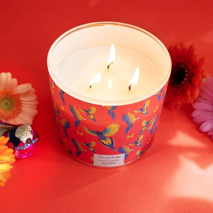 Frida Kahlo “Exotic Jasmine” scented candle with rose-gold lid and vibrant red label featuring colorful parrots and yellow flowers. 