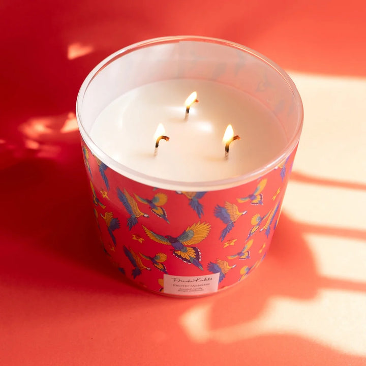Frida Kahlo “Exotic Jasmine” scented candle with rose-gold lid and vibrant red label featuring colorful parrots and yellow flowers. 