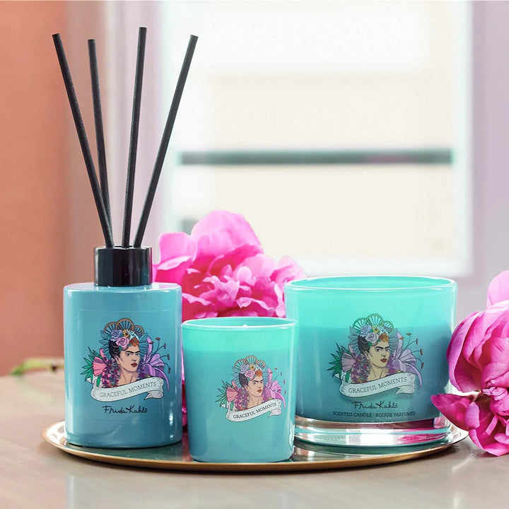 Frida Kahlo Graceful Moments scented candle. Turquoise glass candle featuring an artistic portrait of Frida Kahlo surrounded by colorful flowers and elegant branding.
