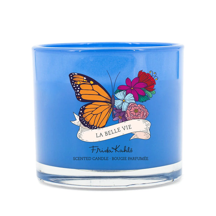 Frida Kahlo La Belle Vie scented candle. Blue glass candle featuring a vibrant butterfly and floral design with elegant Frida Kahlo branding on the front.