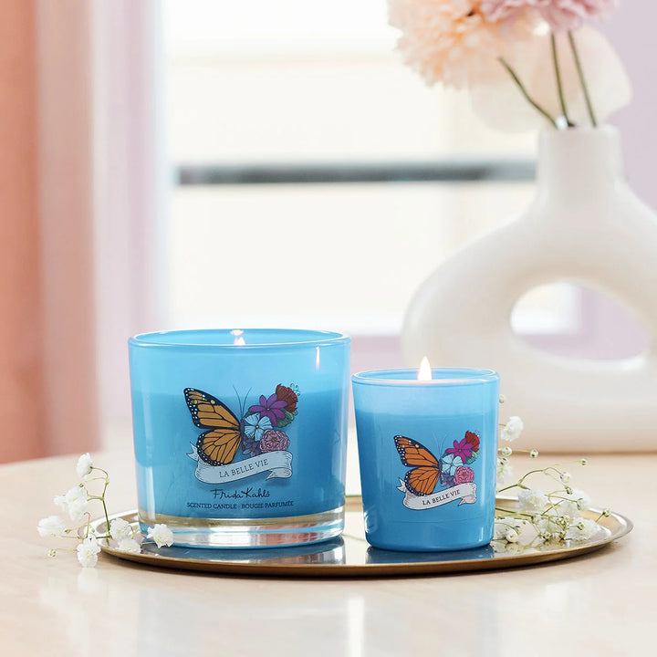 Frida Kahlo La Belle Vie scented candle. Blue glass candle featuring a vibrant butterfly and floral design with elegant Frida Kahlo branding on the front.