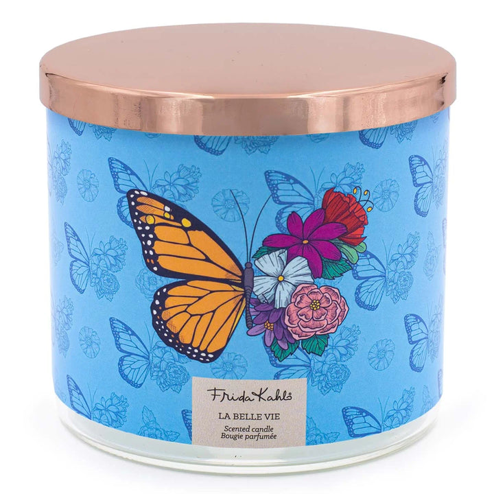 Frida Kahlo La Belle Vie scented candle. Large decorative candle with floral and butterfly design on a blue background and a metallic rose gold lid.