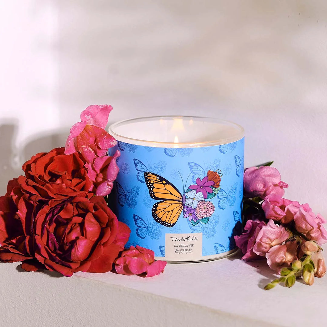 Frida Kahlo La Belle Vie scented candle. Large decorative candle with floral and butterfly design on a blue background and a metallic rose gold lid.