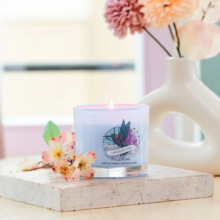 Frida Kahlo Lavender Luxe scented candle.  Elegant purple glass candle featuring a colorful hummingbird and floral design on the front.