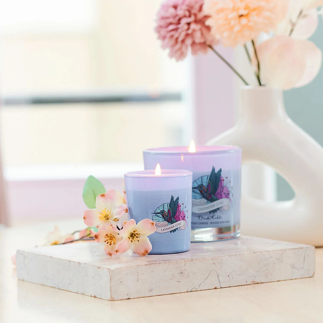 Frida Kahlo Lavender Luxe scented candle.  Elegant purple glass candle featuring a colorful hummingbird and floral design on the front.