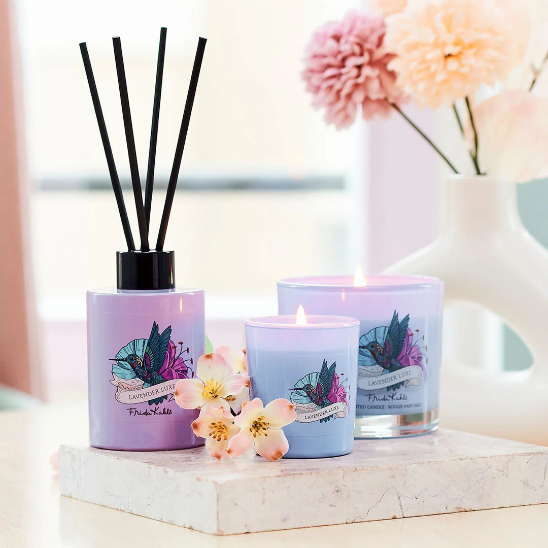 Frida Kahlo Lavender Luxe scented candle.  Elegant purple glass candle featuring a colorful hummingbird and floral design on the front.