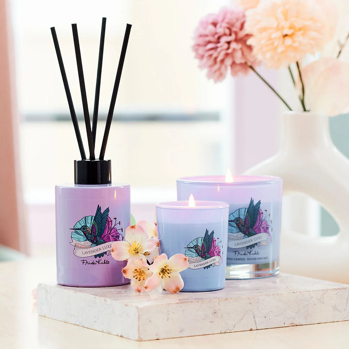 Frida Kahlo Lavender Luxe scented candle.  Elegant purple glass candle featuring a colorful hummingbird and floral design on the front.