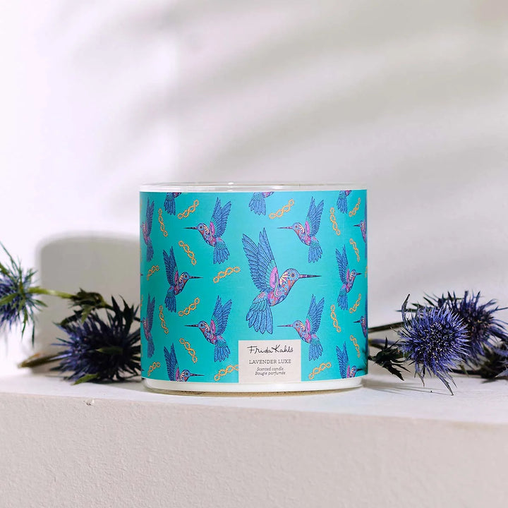 Frida Kahlo “Lavender Luxe” scented candle with a rose-gold lid and turquoise label decorated with colorful hummingbirds. 