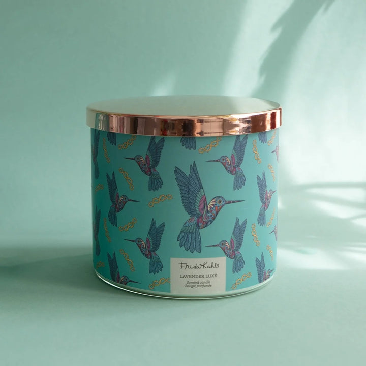 Frida Kahlo “Lavender Luxe” scented candle with a rose-gold lid and turquoise label decorated with colorful hummingbirds. 