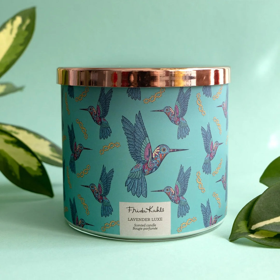 Frida Kahlo “Lavender Luxe” scented candle with a rose-gold lid and turquoise label decorated with colorful hummingbirds. 