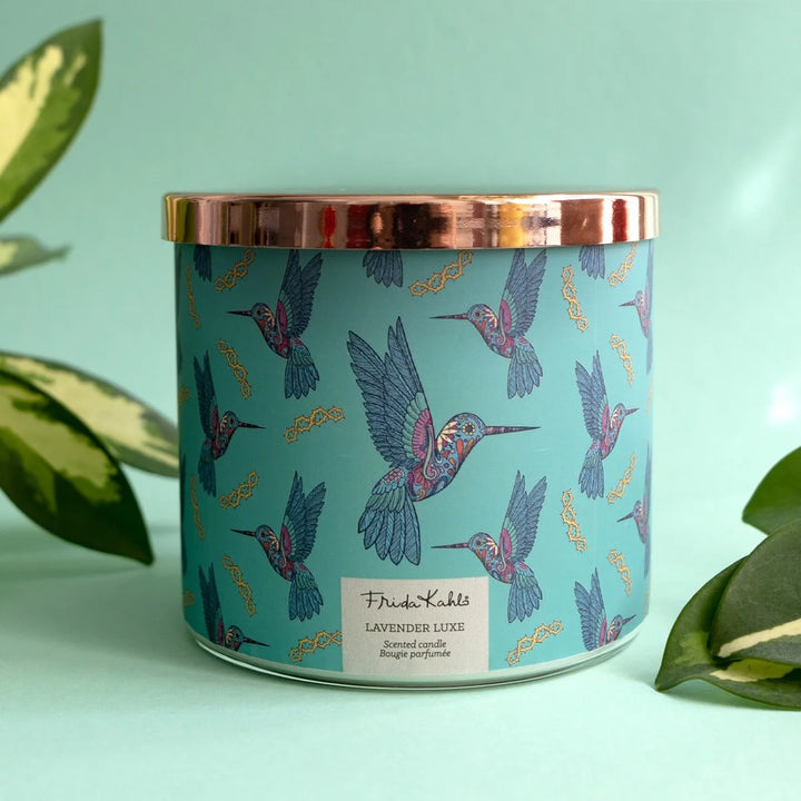 Frida Kahlo “Lavender Luxe” scented candle with a rose-gold lid and turquoise label decorated with colorful hummingbirds. 