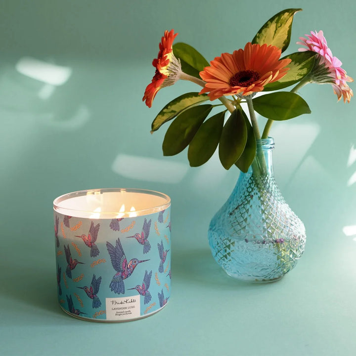 Frida Kahlo “Lavender Luxe” scented candle with a rose-gold lid and turquoise label decorated with colorful hummingbirds. 