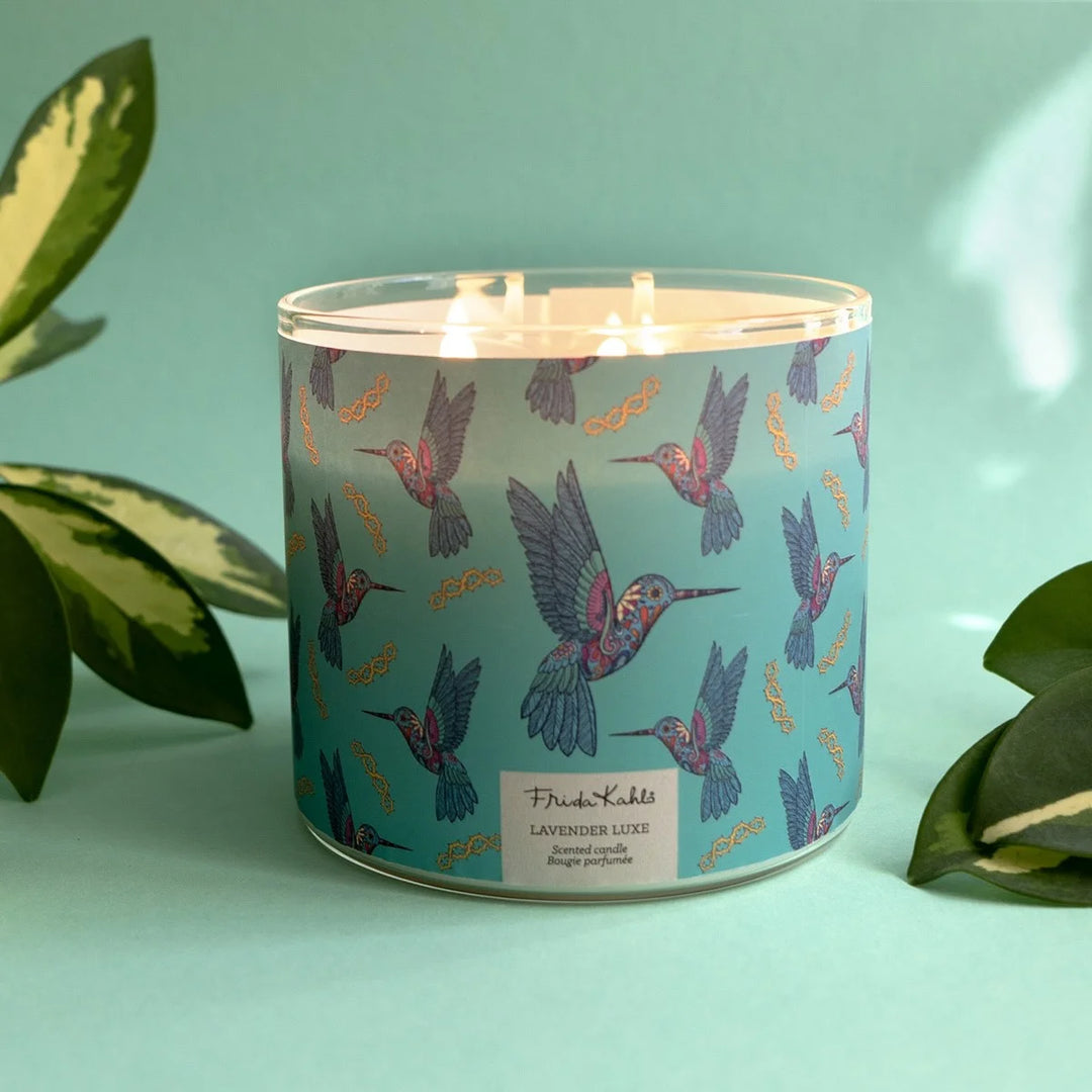 Frida Kahlo “Lavender Luxe” scented candle with a rose-gold lid and turquoise label decorated with colorful hummingbirds. 