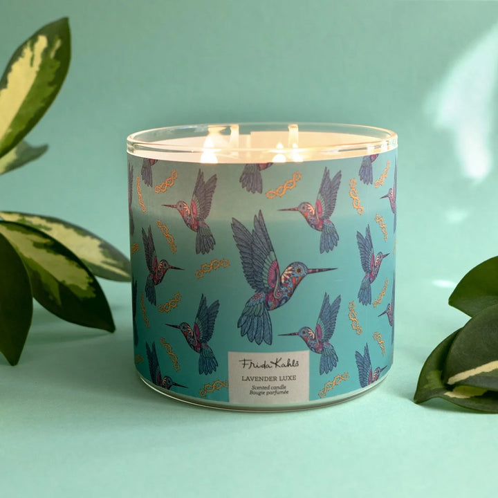Frida Kahlo “Lavender Luxe” scented candle with a rose-gold lid and turquoise label decorated with colorful hummingbirds. 