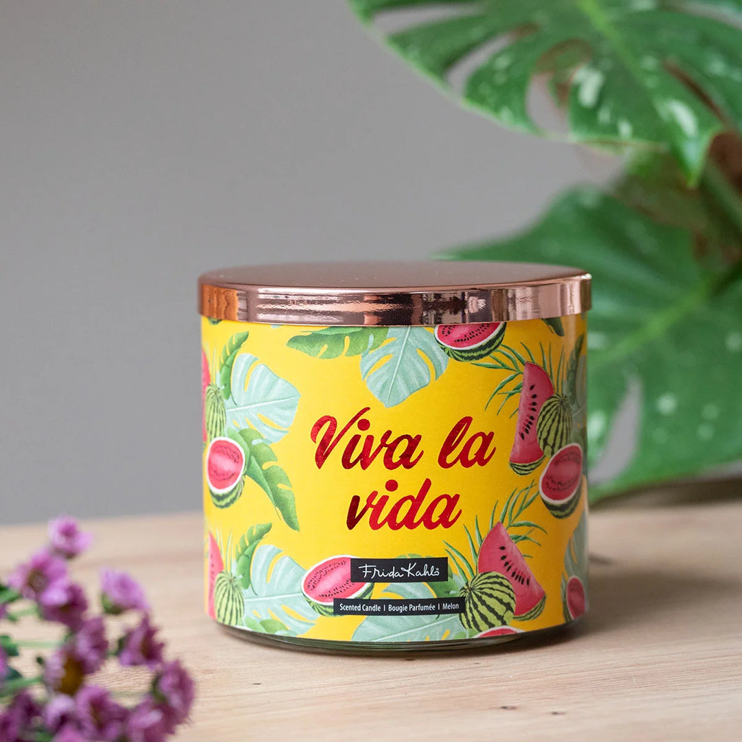 Frida Kahlo “Viva la Vida” scented candle with rose-gold lid and vibrant yellow label featuring watermelon and tropical leaf illustrations. 