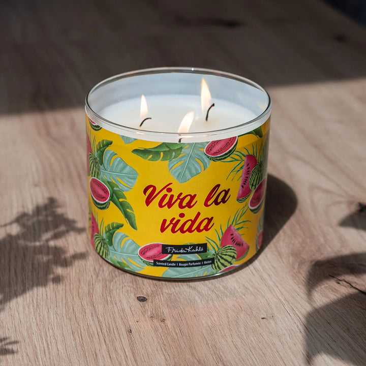 Frida Kahlo “Viva la Vida” scented candle with rose-gold lid and vibrant yellow label featuring watermelon and tropical leaf illustrations. 