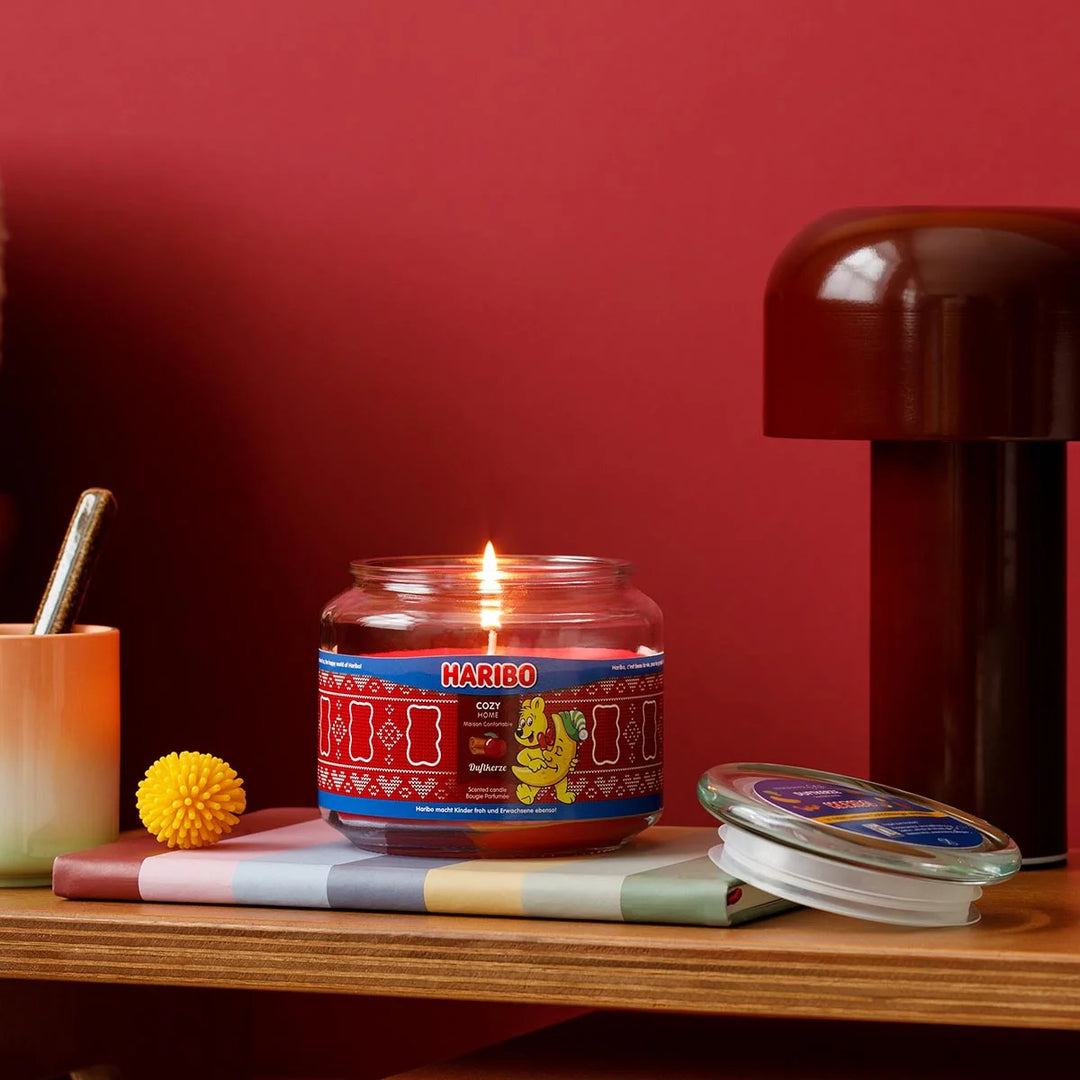 HARIBO Cozy Home scented candle – red jar candle decorated with apple, cinnamon, and the cheerful HARIBO bear holding a moon.