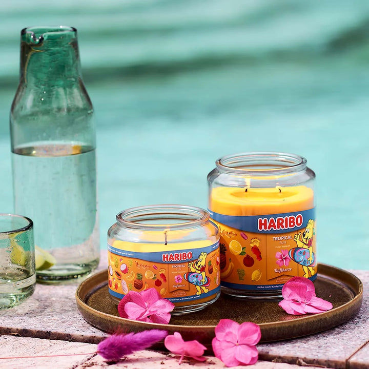 Haribo Tropical Fun Scented Candle in glass jar with lit wick, orange wax and  and fruits design label